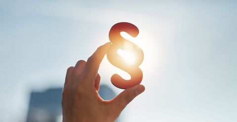Hand die ein Paragraphen Zeichen hält im Gegenlicht der Sonne